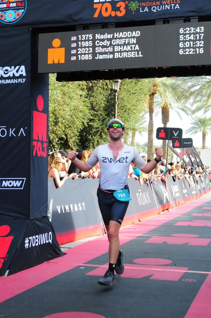 Diego running through the Ironman 70.3 Indian Wells La Quinta finish arch with both fists closed.