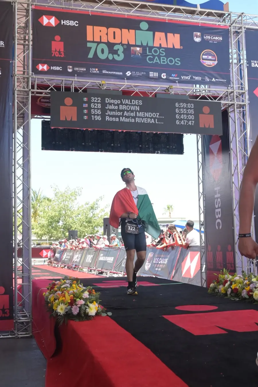 Diego crossing the Ironman 70.3 Los Cabos finish line wrapped in a Mexican flag.